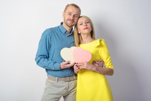 Attractive middle-aged man in a plaid shirt and slender young girl in a yellow dress is holding a heart. Beautiful couple in studio. Loving each other