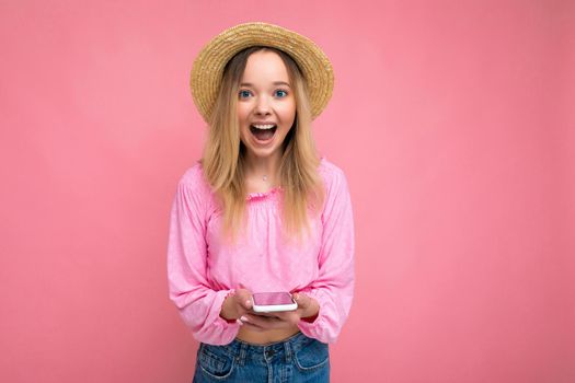 Photo shot of surprised amazed attractive positive good looking young woman wearing casual stylish outfit poising isolated on background with empty space holding in hand and using mobile phone messaging sms looking at camera.