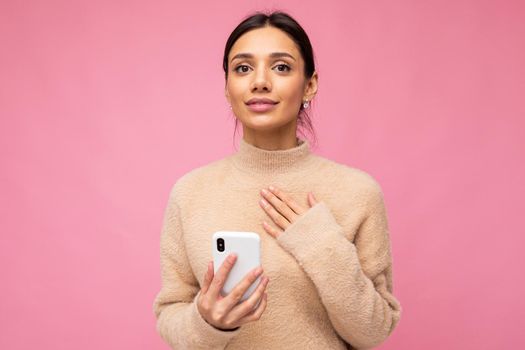 portrait of a gentle brunette on a pink background. holding a phone, looking at the camera.