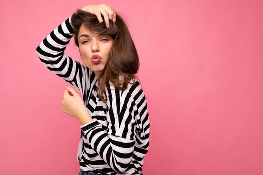 Photo shot of cute attractive pretty happy young brunette woman wearing casual striped longsleeve isolated over colorful background with copy space and giving kiss.