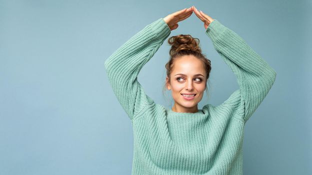 Panoramic photo of young positive happy smiling beautiful woman with sincere emotions wearing stylish clothes isolated over background with copy space and showing home gesture.