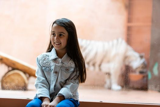 little girl and white tiger behind glass at the zoo