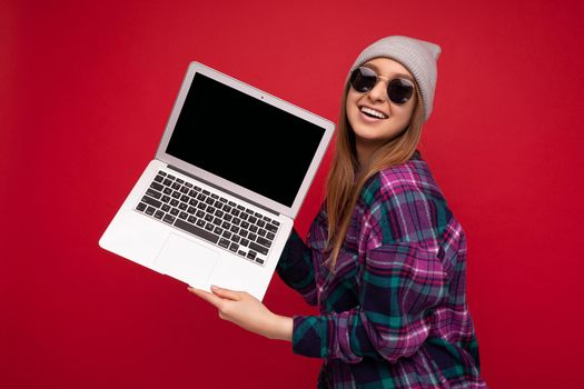 Photo of beautiful young girl holding computer laptop looking at camera isolated over colourful background.