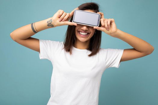 Photo of beautiful smiling young woman good looking wearing casual stylish outfit standing isolated on background with copy space holding smartphone showing phone in hand with empty screen display for mockup.