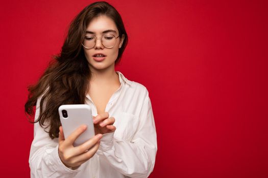 Beautiful young woman wearing casual clothes standing isolated over background surfing on the internet via phone looking at mobile screen.