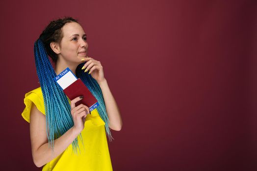 A modern trendy smiling woman in yellow dress with air tickets and a passport in her hand. Young dreamy girl looks aside up. Travel concept