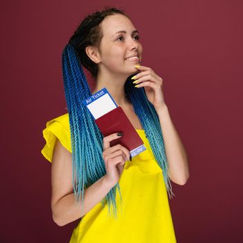 A modern trendy smiling woman in yellow dress with air tickets and a passport in her hand. Young dreamy girl looks aside up. Travel concept