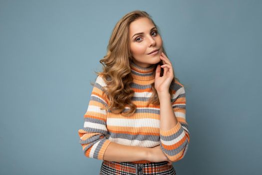 Portrait of young winsome attractive happy sexy blond woman with wavy-hair wearing striped sweater isolated over blue background with empty space.