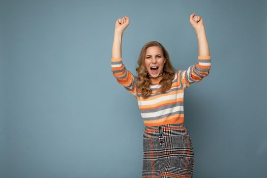 Photo portrait of young pretty beautiful happy positive funny joyful blonde woman with sincere emotions wearing stylish clothes isolated on blue background with empty space and celebrating winning shouting yeah. Victory concept.