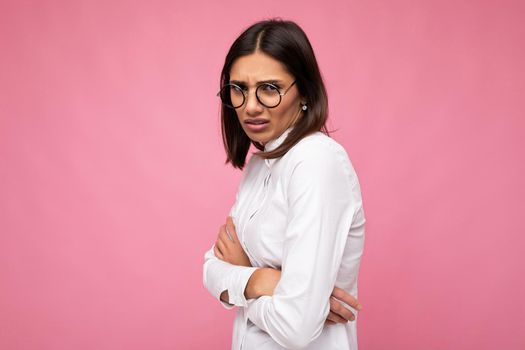 Attractive young offended sad brunette woman wearing everyday stylish clothes and modern optical glasses isolated on colorful background wall looking at camera.