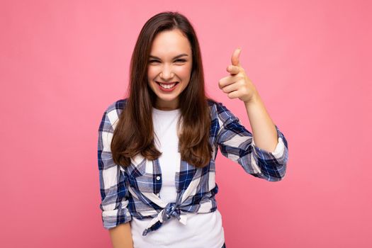 Shot of young happy smiling beautiful brunette woman with sincere emotions wearing trendy check shirt isolated on pink background with empty space.
