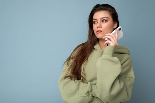 serious upset attractive young woman wearing stylish hoodie holding using mobile phone isolated on background looking to the side.Copy space