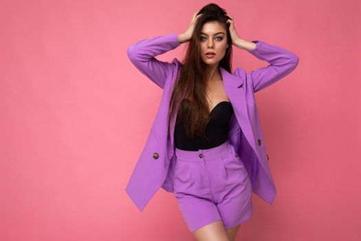 Portrait of young self-confident sexy attractive fashionable brunette woman wearing stylish violet suit isolated on pink background with empty space. Business concept.