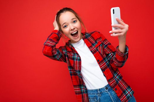 Photo of attractive crazy amazed surprised young woman wearing casual stylish clothes standing isolated over background with copy space holding and using mobile phone looking at camera.