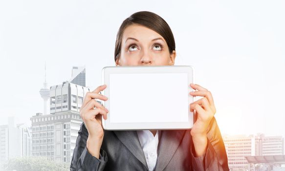 Businesswoman holding tablet computer with blank screen. Beautiful woman in business suit show tablet PC and looking upward. Corporate businessperson on downtown background. Digital technology layout