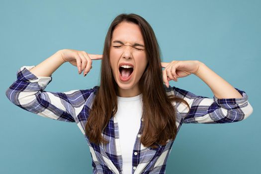 Don't want to hear it, Young emotional attractive brunette female person isolated on blue background with copy space and covering ears and shouting.