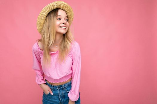 Photo of pretty young female person wearing pink blouse and beige summer hat isolated over pink background looking to the side smilimg and having fun.