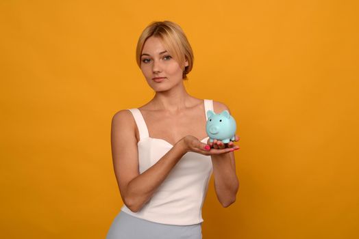 Beautiful young girl holding a pig piggy bank on yellow background. For saving money wealth and financial concept.- image