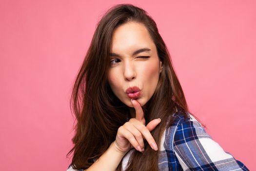 Portrait shot of young positive funny beautiful brunette woman with sincere emotions wearing stylish check shirt isolated on pink background with empty space and thinking.