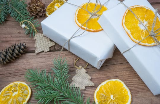 Christmas presents or gift box wrapped in kraft paper with decorations, pine cones, dry orange orange slices and fir branches on a rustic wooden background. Holiday concept