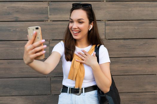 Photo of beautiful happy young woman wearing casual clothes standing in the street having communication via mobile phone looking at smartphone and having fun and good mood.