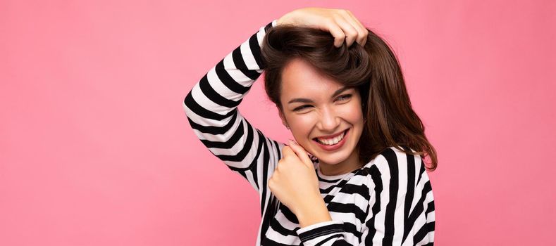 Panoramic photo portrait of young beautiful smiling hipster brunette woman in trendy pullover. Sexy carefree female person posing isolated near pink wall with empty space in studio. Positive model with natural makeup.