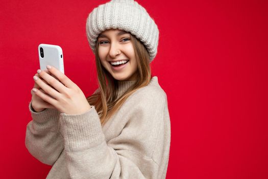 closeup Photo shot of attractive smiling positive good looking young woman wearing casual stylish outfit poising isolated on background with empty space holding in hand and using mobile phone messaging sms looking at camera.