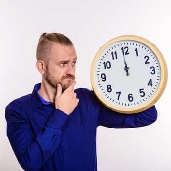 A stylish man thinks out the idea and holds a large wall clock on white background