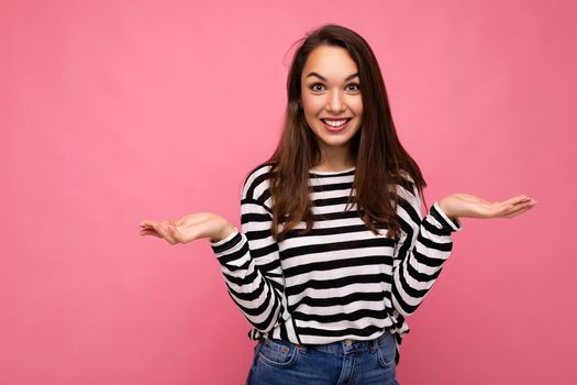 Photo of young positive happy beautiful brunette woman with sincere emotions wearing casual striped pullover isolated on pink background with copy space.