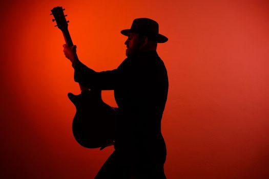 silhouette of a musician playing instrument in a hat on a red background