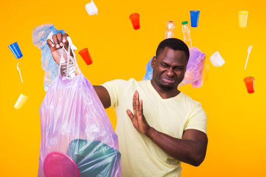 Environmental pollution, plastic recycling problem and waste disposal concept - angry man holding garbage bag on yellow background. He is feel smell of trash.