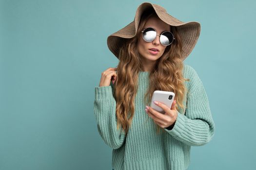 girl in a hat and sunglasses on a blue background with a phone in her hands.