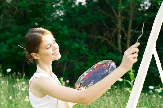 woman artist outdoors with palette of paints paints a picture. High quality photo