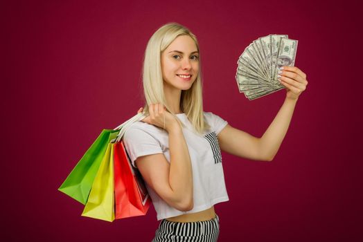 Happy girl in holds one hundred dollars bills and shopping bags on ruby background