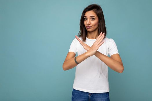 Portrait of young beautiful brunette woman with sincere emotions wearing trendy white t-shirt for mockup isolated on blue background with empty space and showing stop gesture.