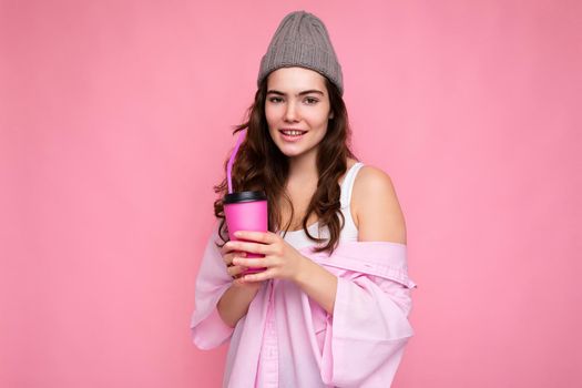 Beautiful young positive brunette woman wearing casual stylish clothes isolated over colorful background wall holding paper cup for mockup drinking coffee looking at camera.