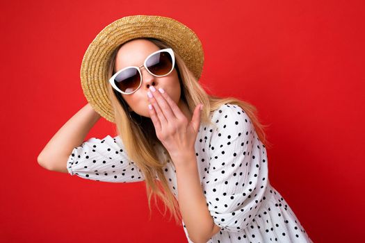 Attractive young blonde woman wearing everyday stylish clothes and modern sunglasses isolated on colorful background wall looking at camera and giving kiss.