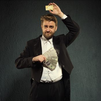 Positive man in a tailcoat offers a credit card and money. - image