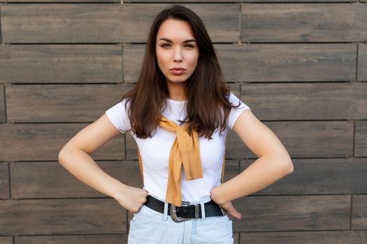 Portrait of touchy sad upset offended young brunet woman wearing casual white t-shirt and jeans with yellow sweater poising near brown wall in the street.