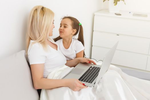 Smiling mother and daughter using laptop in bed at home