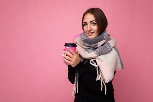 Beautiful young positive brunette woman wearing casual stylish clothes isolated over colorful background wall holding paper cup for mockup drinking coffee looking at camera. copy space