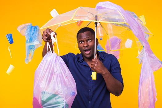 Problem of trash, plastic recycling, pollution and environmental concept - surprised man carrying garbage bag on yellow background.