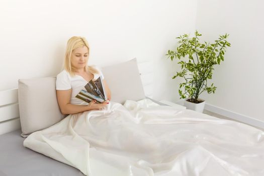 Woman holding with photo book and sitting on bed