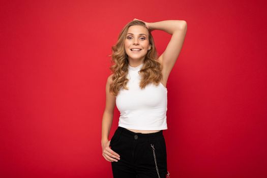 Photo of young charming fascinating sexy attractive happy smiling delightful blonde woman with sincere emotions wearing stylish clothes posing isolated over red background with copy space.