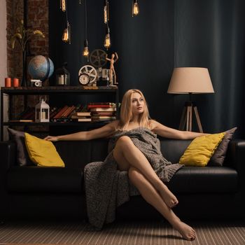 winter concept - young woman sitting on sofa in warm blanket