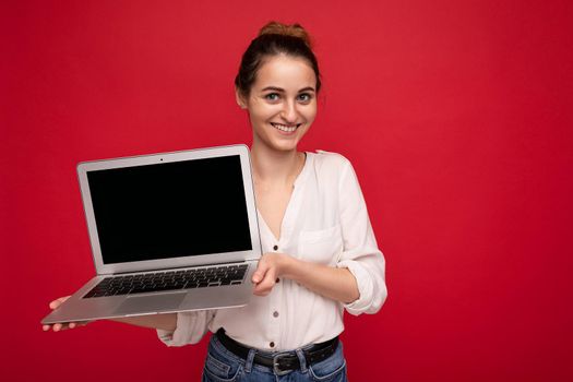 Photo of beautiful young woman holding computer laptop looking at camera isolated over colourful background.