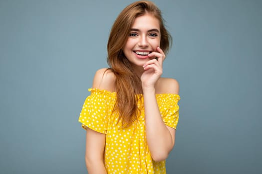 Young smiling beautiful dark blonde woman with sincere emotions isolated on background wall with copy space wearing stylish summer yellow dress. Positive concept.