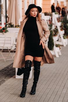 Stylish young woman in a beige coat in a black hat on a city street. Women's street fashion. Autumn clothing.Urban style.