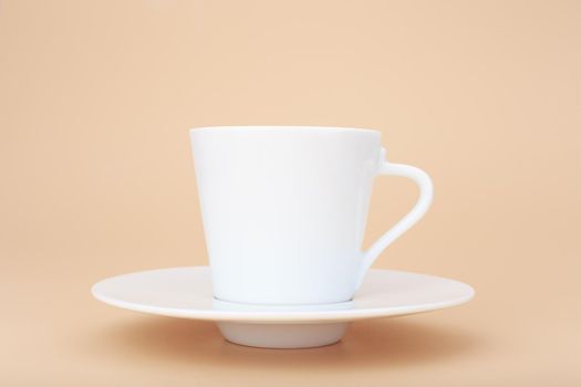 White ceramic coffee cup with saucer against pastel beige background with copy space. Concept of hot drinks, ceramic cups and kitchen utensil