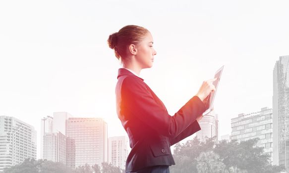 Young businesswoman using tablet computer. Double exposure concept with modern cityscape and beautiful woman in business suit. Digital technology in property management and development company.